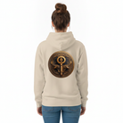 A woman viewed from behind wearing a light beige hoodie with a large circular gold and dark blue key graphic printed on the back, paired with blue jeans against a plain white background.